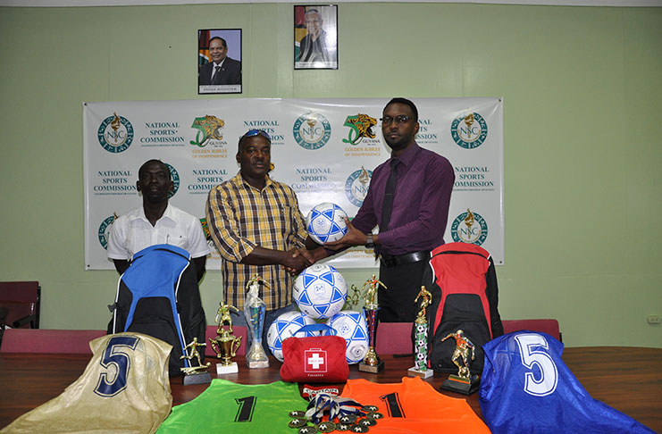 Director of Sport,Christopher Jones hands over one of the customized balls to EBFA President,Franklin Wilson in the presence of association secretary,Wayne Francois. The other equipment is on display