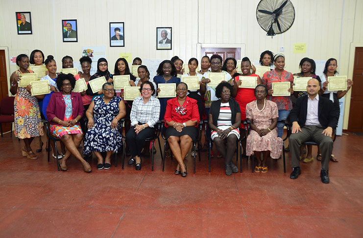 First Lady Mrs Sandra Granger celebrates with the graduates, who are pictured standing. In the front row from left to right are, Ms Yvonne Smith of the Office of the First Lady; Ms Ismay Griffith, Licensed Clinical Social Worker and Facilitator ; the First Lady; Ms Lorene Baird, Permanent Secretary, Ministry of Social Protection ; Ms Hazel Halley-Burnett, Gender Consultant at the Ministry of Social Protection; Ms Venus Smart, Public Health Nurse and Mr Diego Alphonso, Head of the Men's Affairs Bureau, Ministry of Social Protection