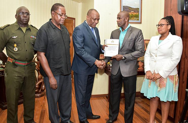 Minister of State, Joseph Harmon receives the report from Brigadier (Retired) Bruce Lovell as Lieutenant Colonel Denzel Carmichael, former Assistant Commission of Police, Mr. Winston Cosbert and Ms. Christine Bailey look on.