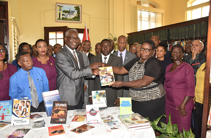 In front row, President of the Caribbean Union of Seventh-day Adventists, Dr. Kern Tobias, presents a sample of the books to Chief Librarian, Emily King
Others from left are: Michael Kendall, treasurer of the Guyana Conference of SDAs and Pastor Exton Clarke, executive secretary (Guyana Conference) along with other staff of the National Library. At right are pastors, executives and other functionaries attending the Annual Caribbean Union Mid-Year Executive Committee meeting in Guyana