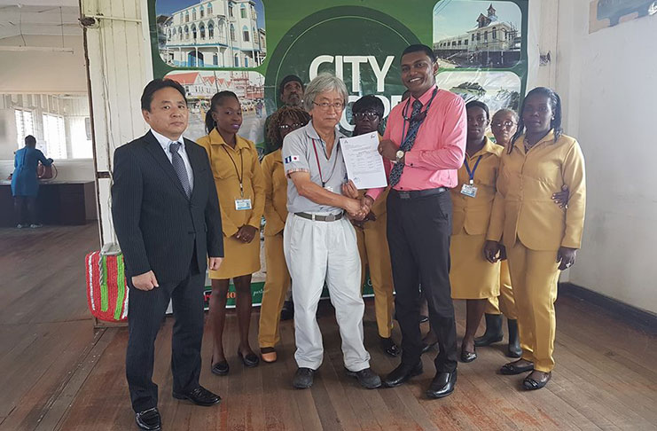 JICA Volunteer Takamasa Eda (at centre) through Senior Resident Officer Minoru Ito (first from left), makes a presentation to Solid Waste Management Director Walter Narine and staff of the department