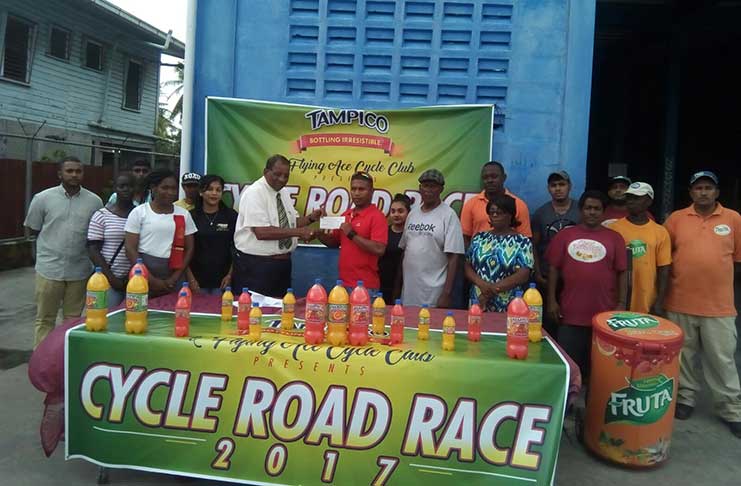 General Manager of the Guyana Beverage Company, Robert Selman, hands the sponsorship package to Neil Reece. Organiser and coach Randolph Roberts pose with other executives of the FACC, staff of the GBC, cyclists and parents as they share the moment.