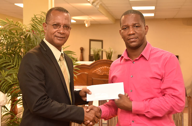 COURTS Marketing Manager Pernell Cummings (right) makes a presentation to AAG president Aubrey Hutson following year day’s launch of the COURTS 10K. (Adrian Narine photo)