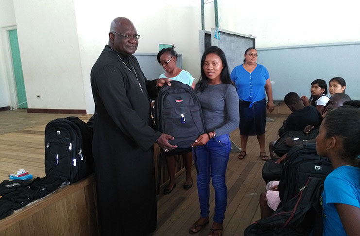 Anglican Bishop of Guyana, Suriname and Cayenne, the Right Reverend Charles Davidson, hands over a backpack to one of the students of the Linden Foundation Secondary School as others look on