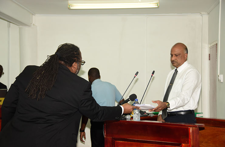 Attorney Selwyn Pieters passes a document to Police Commissioner, Seelall Persaud, on Monday during his testimony at the CoI.