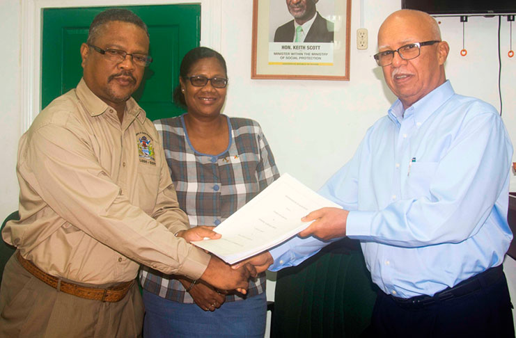 Mr. Clifford B. Reis Chairman/Managing Director of Banks DIH Limited presents a copy of the Agreement to Mr. Charles Ogle, Chief Labour Officer, in the presence of a Department of Labour official.