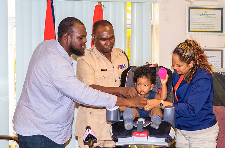 GNRSC Coordinator Ramona Doorgen and Traffic Chief Dion Moore handed over a car seat to Road Safety Council volunteer Mikoowanyah Yosef-Yisrael and his daughter as part of the campaign to educate society on the laws of child restraint (Delano Williams Photo)