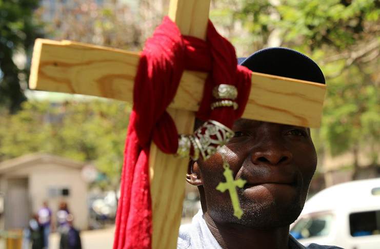 A resident holds a cross as he attends a prayer meeting called to force Zimbabwean President Robert Mugabe to resign outside Parliament Building in Harare, Zimbabwe (REUTERS)