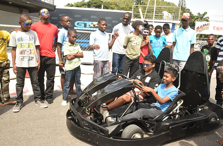 125cc competitor Mikhil Persaud shows one of the children how to use the kart. (Adrian Narine photos)