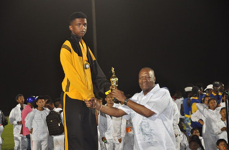 Minister of State Joseph Harmon makes a presentation District 10’s Murphy Nash at the closing ceremony of the National Schools athletics, swimming and track and field championships. (Delano Williams photo)