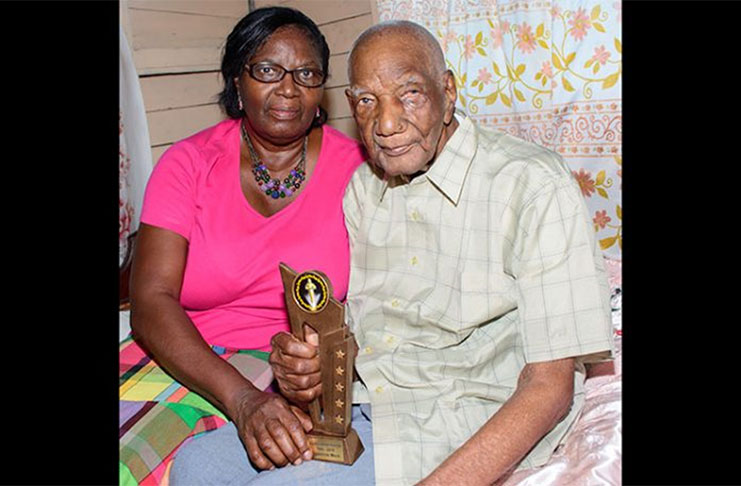 Mr. Gladstone Mack, who recently celebrated his 106th birthday. In his right hand is the award he received last year from the Government of Guyana during Independence Jubilee celebrations for being the oldest surviving man in Guyana. At left is his eldest daughter, Mrs. Winifred Camacho (Photo by Samuel Maughn)