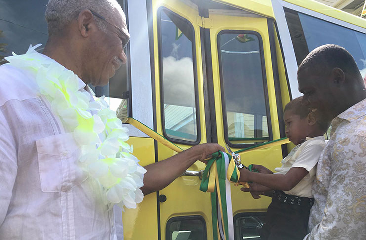 President David Granger is assisted by this lad of Fyrish Primary School to cut the ceremonial ribbon to commission the school bus