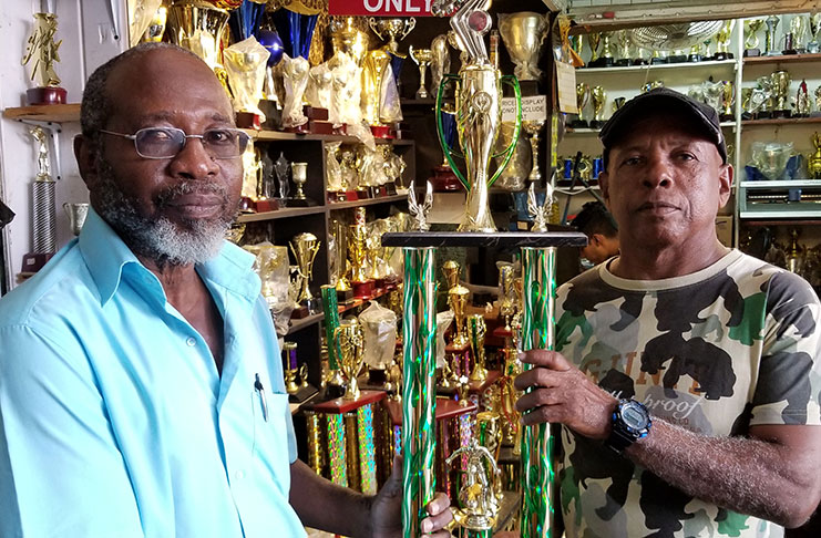 In photo, Trophy Stall’s Graphic Artist and former Pele Football Club player, Brian Sealey (right), hands over the winning trophy to tournament organiser Lennox Arthur.