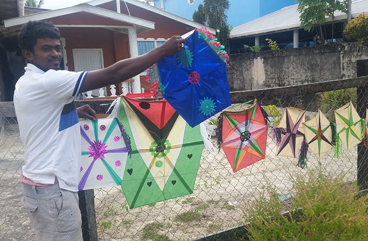 Adit Ramanand standing in front his yard where he sells his kites. He is posing with some of the kites he made