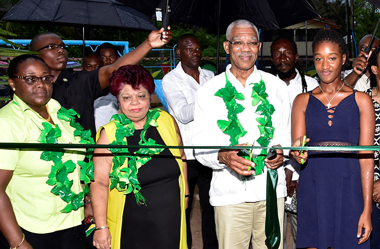 President David Granger is assisted by a youth of Victory Valley to cut the ceremonial ribbon to declare open the Victory Valley Play Park. Looking on from left are Ministers Simona Broomes and Amna Ally.