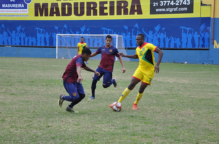 Guyana’s Kevin Layne is closely watched by this Madureira duo.