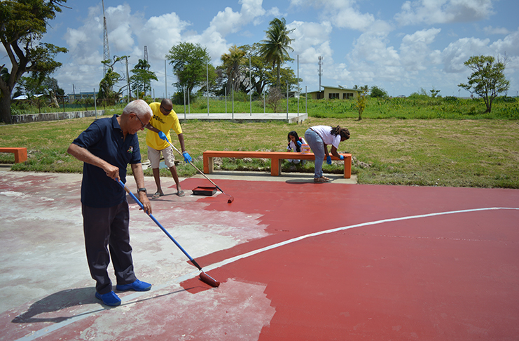 Massy's Chairman, Deo Persaud (at left) along with staff assisting in repainting the basketball court and benches during their 50th anniversary celebrations