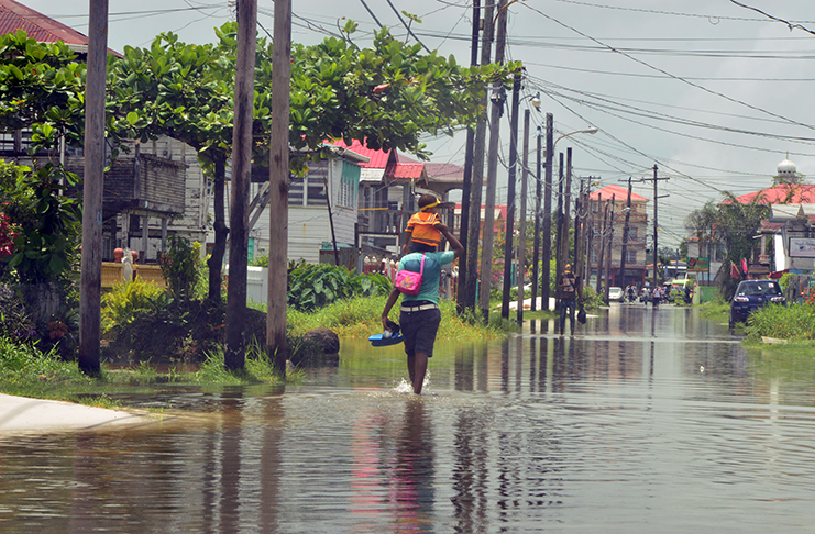 Residents wade through floodwaters in Alexander Village on Tuesday (Adrian Narine photo)
