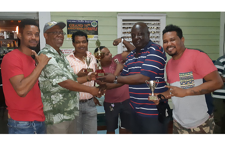 Frederick Halley, second left, hands over the winning trophy to Ian John, a member of the victorious team in the presence of other members.