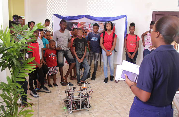 Children at the ‘Reading and Robotics’ programme at the National Library, looking on at a demonstration of the STEM Guyana robot that participated in the First Global Robotics championships this year (Vishani Ragobeer photo)