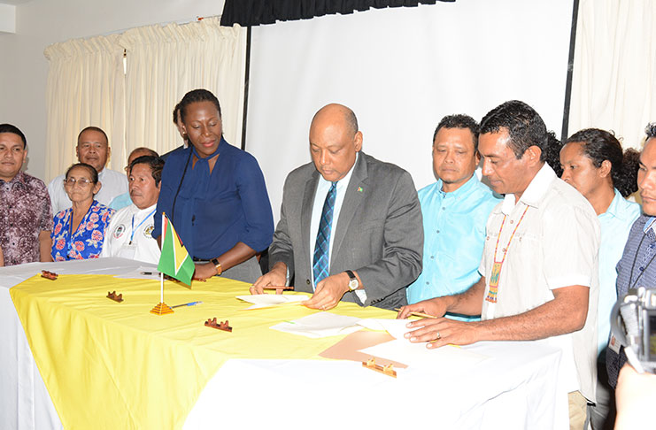 Minister of Natural Resources Raphael Trotman, NTC Chairman Toshao Nicholas Fredricks and Director of Environment Ndibi Schwiers sign the MOU while being flanked by Toshaos.