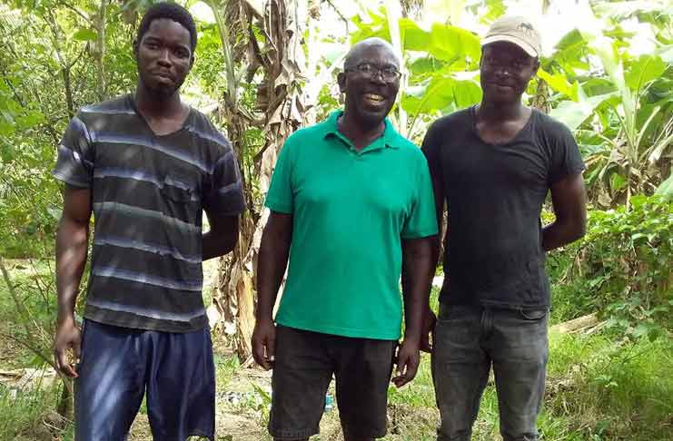 Reginald Daniels posing with the young farmers, Ceon Samuels and Delvin Thompson in the backlands on their farm