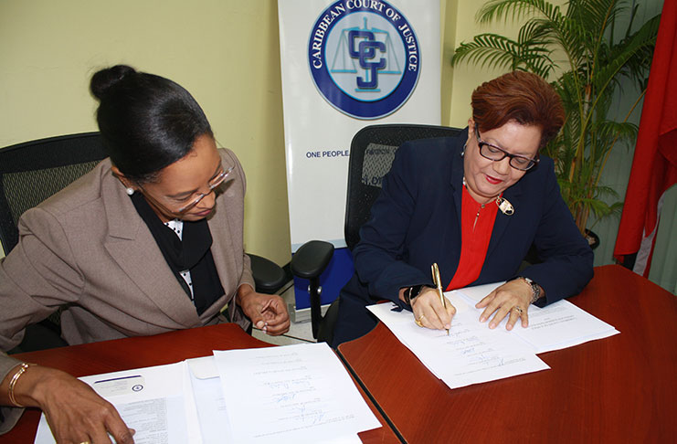 Registrar and Chief Marshal of the Caribbean Court of Justice, Ms. Jacqueline Graham watches as the Hon. Mme. Justice Maureen Rajnauth-Lee affixes her signature to the revised Rules of Court in the Original and the Appellate Jurisdictions