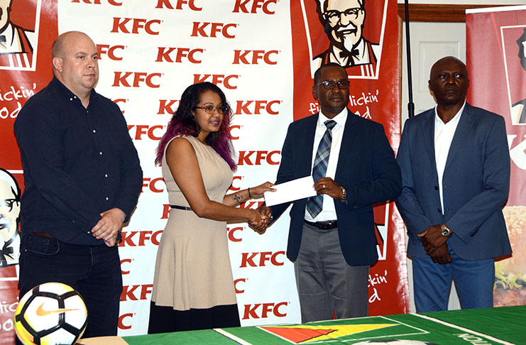Charissa Rampersaud, KFC Guyana Training Manager presents GFF president Wayne Forde with a cheque for an undisclosed sum, while GFF’s Ian Greenwood (first from left) and Competitions Director Ian Alves look on. (Adrian Narine photo)