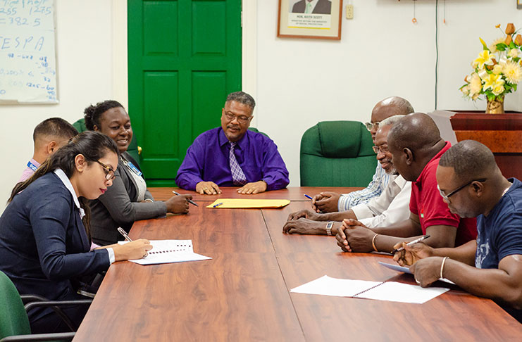 Chief Labour Officer, Charles Ogle, (centre) watches on as representatives from the CCWU (sitting right) and representatives from the CJIA (sitting left) sign on to the new agreement (Delano Williams photo)