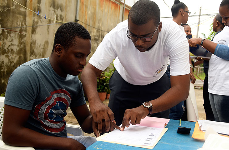 A GECOM enumerator assists 20-year-old Joel Evans in the registration process (Adrian Narine photo)