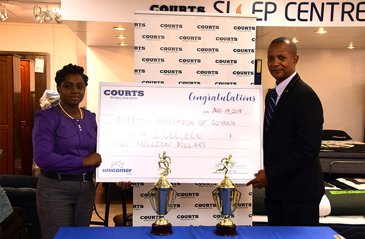 COURTS Marketing Manager, Odetta Aaron (left) makes a presentation to AAG president, Aubrey Hutson, to mark the launch of the COURTS 10k. (Adrian Narine photo)