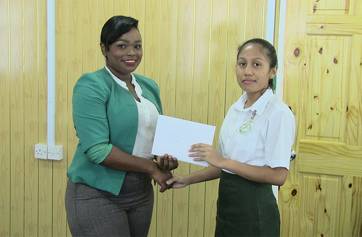 CSEC top performer, Riana Toney, as she uplifted her cash prize from Pinnacle Communications representative Ava Thompson