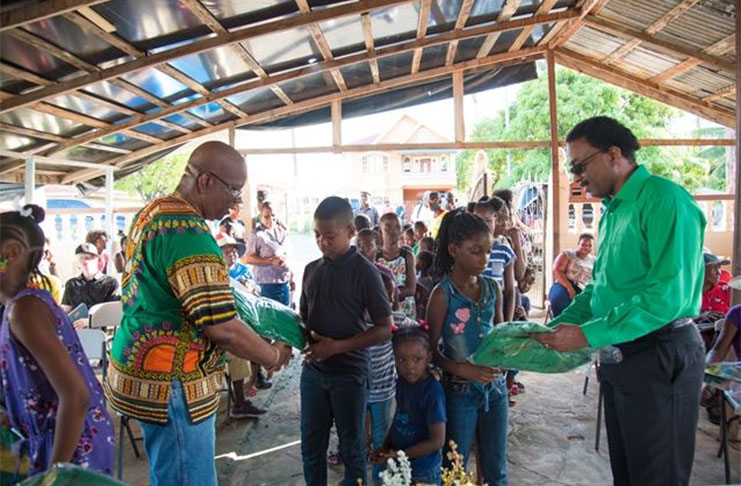 Minister of Finance Winston Jordan and Attorney-General and Minister of Legal Affairs, Basil Williams, distributing schoolbags to children of Litchfield Village