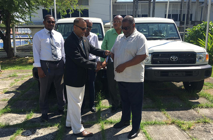 Officer-in-Charge at UNDP Guyana, Navindra Persaud (in jacket), presents the keys to two Toyota Land Cruisers to government's representative on the project, Permanent Secretary Derrick Cummings.  Project Co-ordinator, Phillip Walcott and other officers look on (Ministry of Public Telecommunications photo)