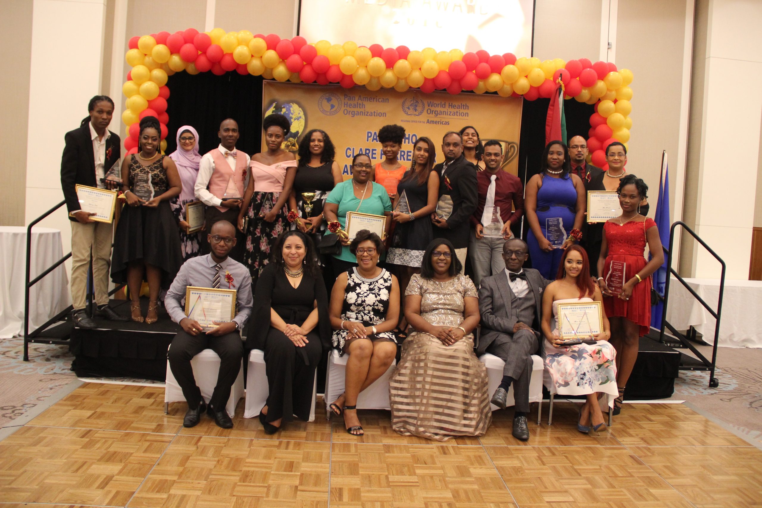From L-R: PAHO/WHO 2018 overall winner for Excellence in Health Journalism, Handell Duncan; Chief Judge, Dr Paloma Mohamed; Minister of Telecommunications, Catherine Hughes; Minister Karen Cummings; Dr William Adu-Krow and Newsroom Journalist Bibi Khatoon. Standing, are the other awardees. 