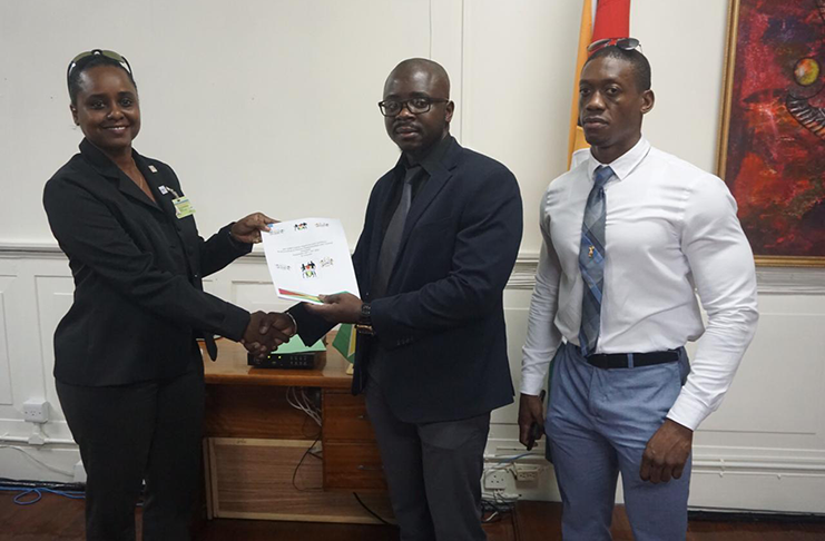 GABFF   president Keavon Bess presents the financial document to Assistant Director of Sport, Melissa Dow-Richardson with CAC gold medallist Kerwin Clarke (far right) in their company.