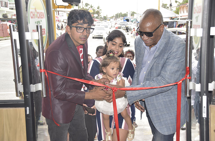 Director General, Joseph Harmon assists the owners of the food entity to cut the ribbon to officially open the business