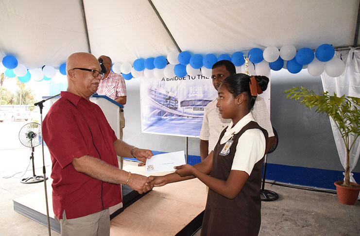 Banks DIH Chairman Clifford Reis handing over the cheque for the C. V. Nunes Primary to one of its pupils