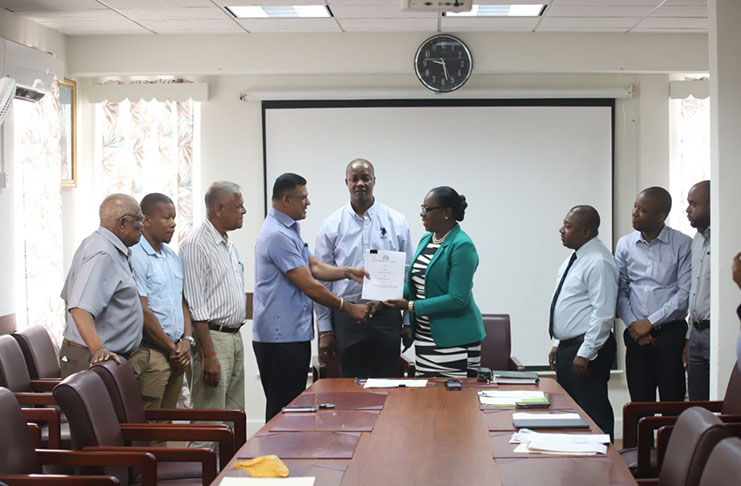 Education Minister Dr Nicolette Henry hands over the contract to Brian Tiwari in the presence of his team and other education officials