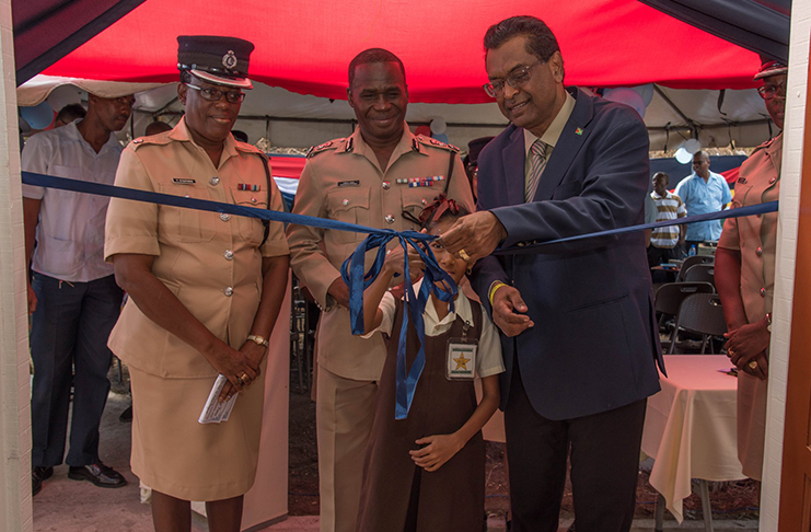 Minister Khemraj Ramjattan assists a school child from the district to cut the ceremonial ribbon to recommission formally, the Number 10 Police Outpost in Mahaica, ECD. Also looking on are Commissioner Leslie James and Divisional Commander Superintendent, Yonette Stephens