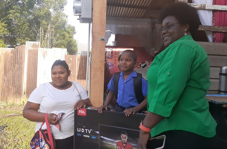 Minister within the Ministry of the Presidency with responsibility for Youth Affairs, Simona Broomes, presenting Jonathon McLennan and his mother, Samantha Salvador, with a new television set on behalf of a donor who requested to remain anonymous