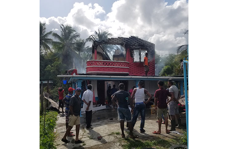 Neighbours look on at the ruined remains of the Seepersaud’s home (Tamica Garnett photo)