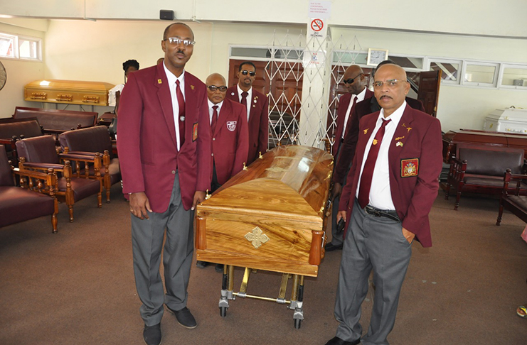 Claude ‘Alfy’ Duguid’s buddy, captain Mahendra Persaud (right); secretary Ryan Sampson (left) and other teammates stand alongside the remains of their longtime shooting pal at the Merriman Funeral Home Inc., yesterday.