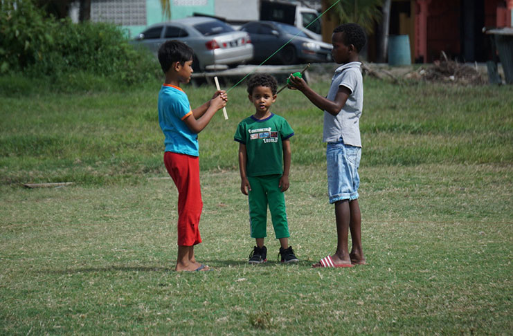 Three children on the field near Laing Avenue engaging in their kite-flying activity