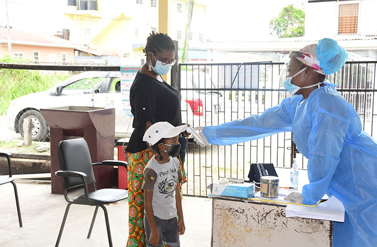 A woman’s son receives a temperature check at the first triage at the screening/sample-collecting centre established at the Herstelling Health Centre (Adrian Narine photo)
