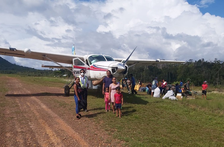 A Trans Guyana pilot stands alongside Region 8 residents at Mahdia. (TGA photo)