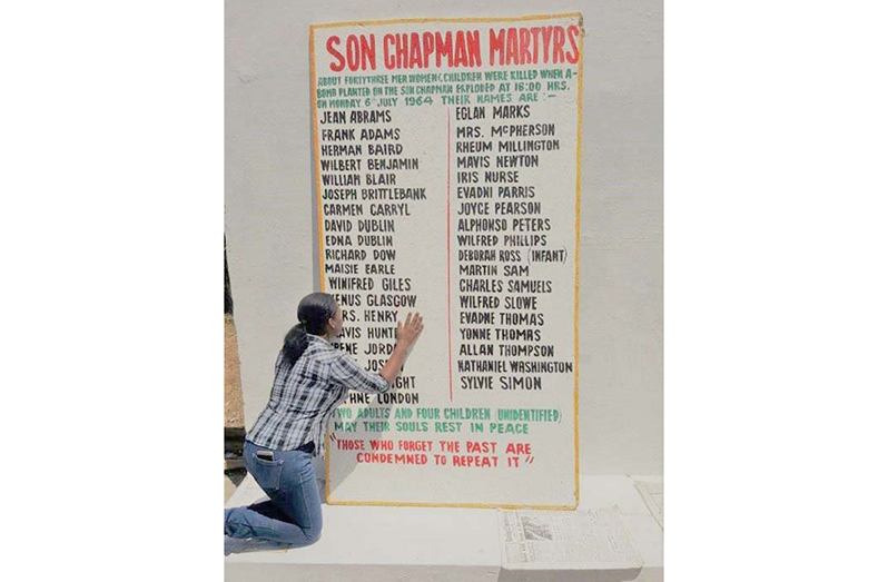 Diana Chapman looks at the painted board with names of persons who perished in the massacre