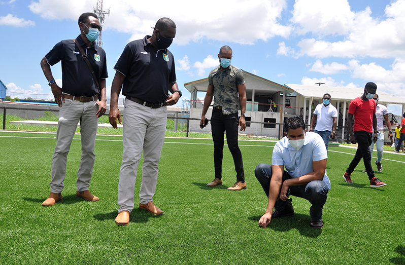 GFF president Wayne Forde (2nd left) observes as Minister Ramson gets a feel of the turf at the GFF National Training Facility. (GFF photo)