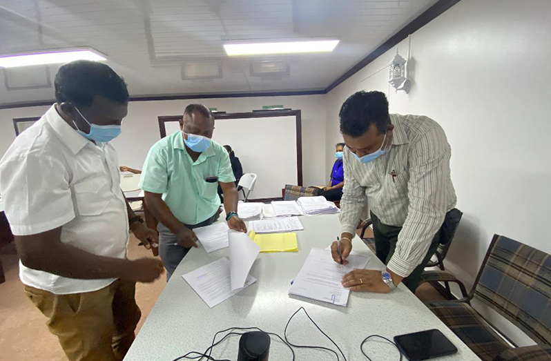 Regional Executive Officer (REO) Devanand Ramdatt (right) signing contract documents as the contractor who won the award (left) looks on. Also pictured is Secretary of the Regional Tender Board (RTB), Elroy Stephney.