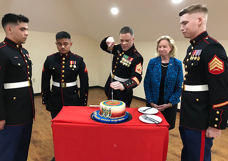 A marine guard cuts the anniversary cake in the presence of Ambassador Sarah-Ann Lynch and his colleagues
